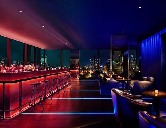 A lively bar counter featuring RGBW lighting effects, controlled remotely to change the color and ambiance of the space. The lighting under and behind the shelves adds a colorful, energetic vibe.