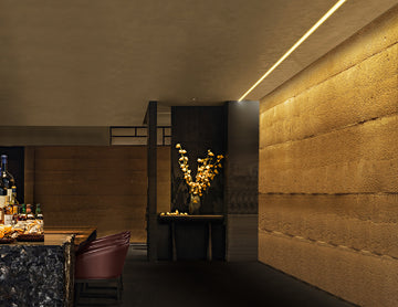 A recessed aluminum fixture runs along the edge of the restaurant ceiling near the wall, projecting a soft 2700K warm white glow. Its angled design gently washes the wall with light, adding depth and a cozy ambiance. Seamlessly built into the ceiling, it maintains a clean, modern look that complements the dining space.