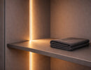 Recessed aluminum undercabinet LED strip light integrated into cabinet shelf, creating warm 3000K vertical architectural lighting effect for closet and display applications.