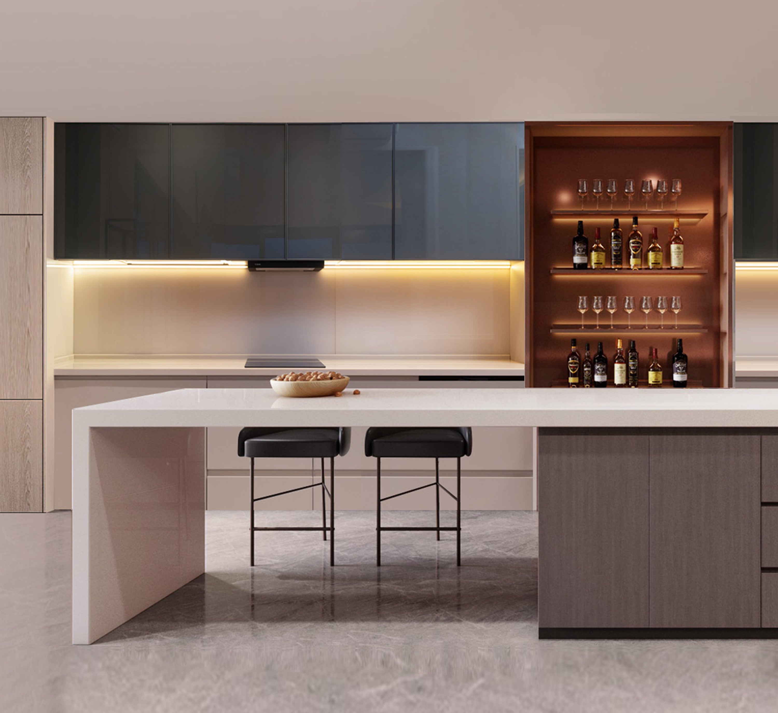 A contemporary kitchen with under-cabinet lighting highlighting a sleek, grey cabinetry with a reflective backsplash and a white stone countertop. An open display cabinet with internal lighting presents an array of liquor bottles and glasses, while two modern black bar stools sit at the kitchen island, and a bowl of bread adds a homely touch.