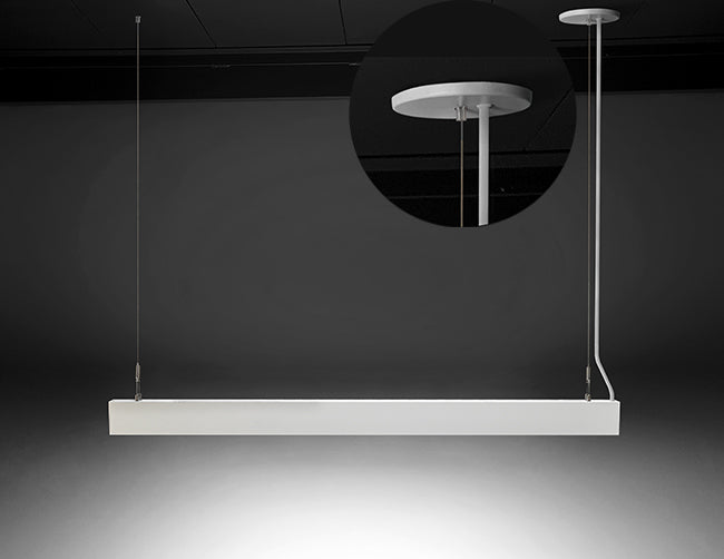 A white color GL LED L8456 linear light fixture is suspended from a ceiling, with one side using a white canopy for both a suspension cable and a power cable to go through, and the other side with a suspension cable without a canopy.